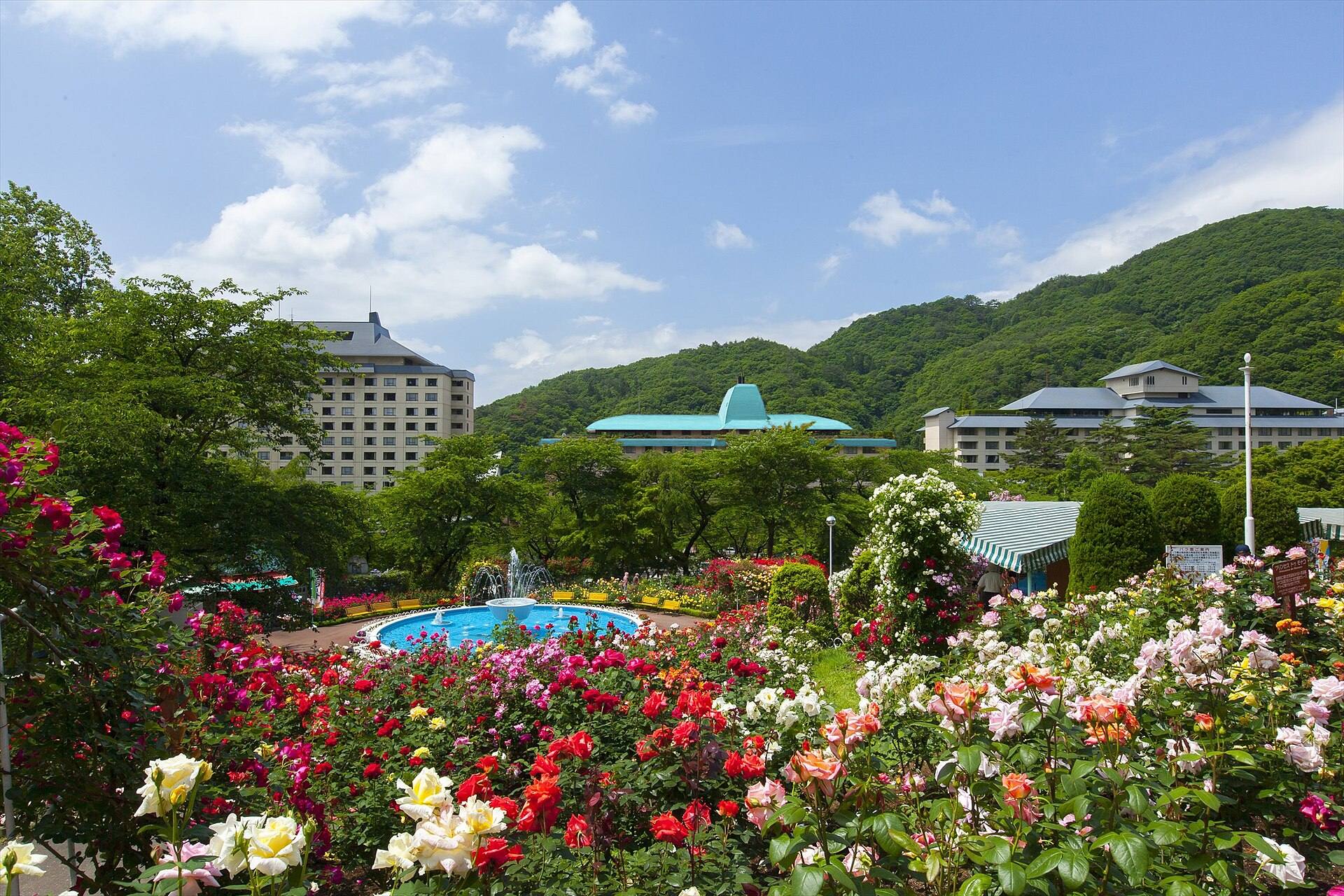 Roses and a fountain below the Hanamaki Onsen hotels and wooded hills.