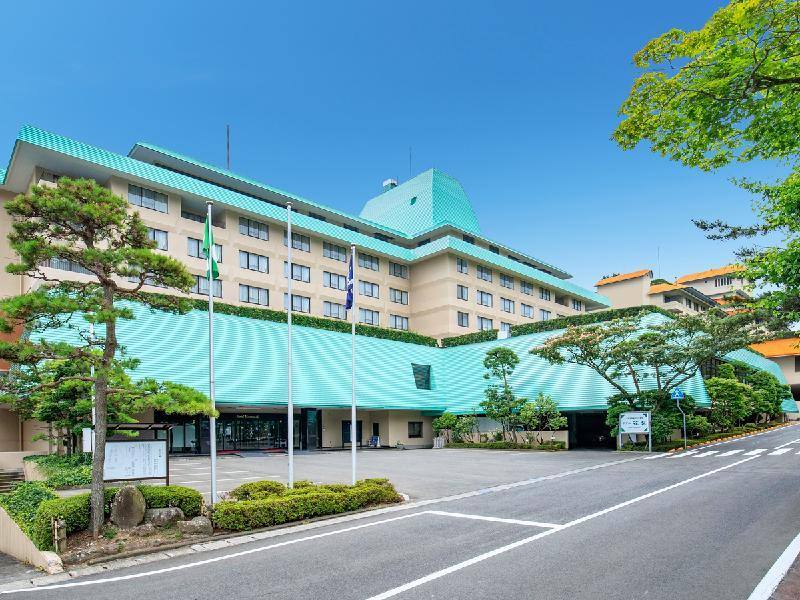 Hanamaki Onsen Hotel Hanamaki with a green roof beside a tree-lined road