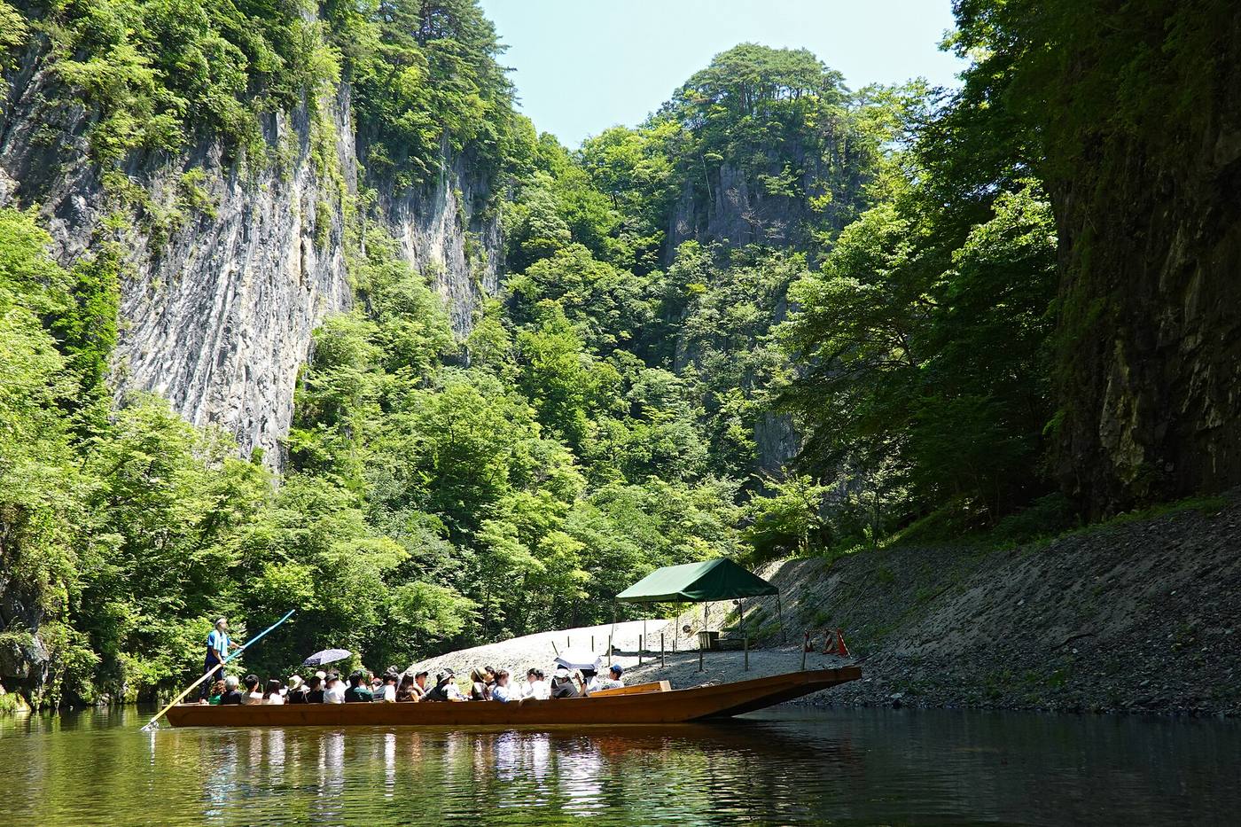 A flat-bottom sightseeing boat beneath the green limestone cliffs of Geibikei Gorge.
