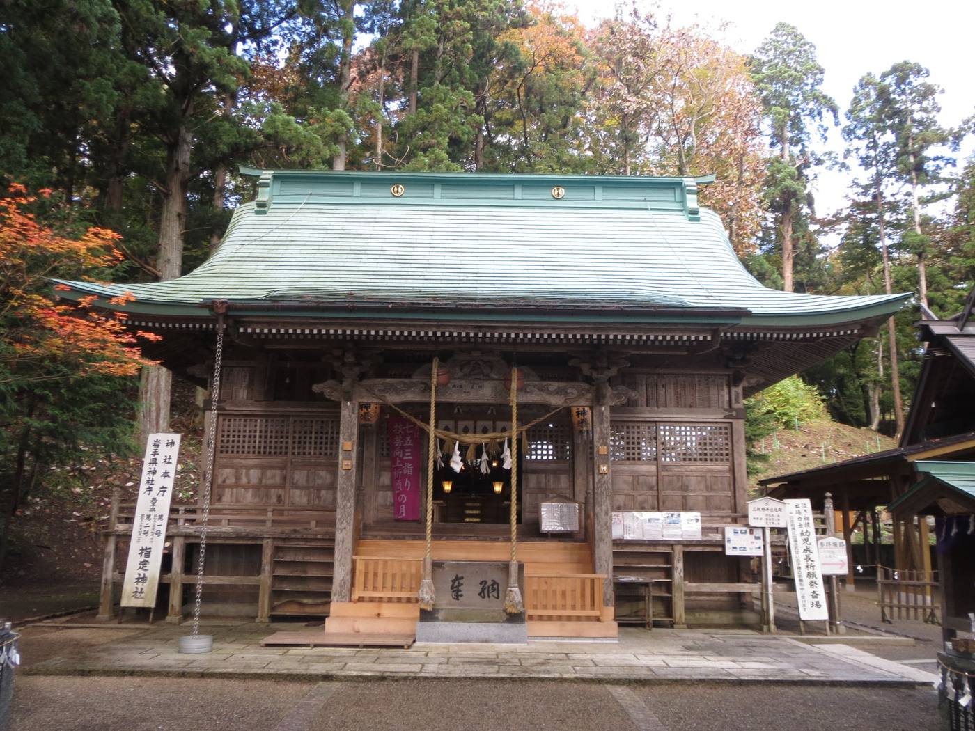 Mikumano Shrine’s wooden worship hall with a green roof and autumn foliage.