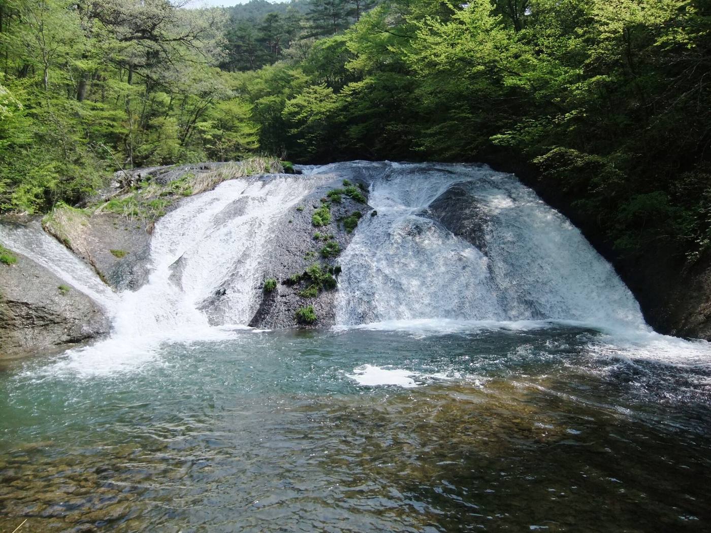 Kamabuchi Falls flowing over a broad rock face in the woods at Hanamaki Onsen.